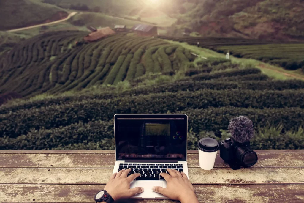 Eine Person, die einen Laptop auf einem Tisch mit einer Kamera und einer Tasse Kaffee benutzt.